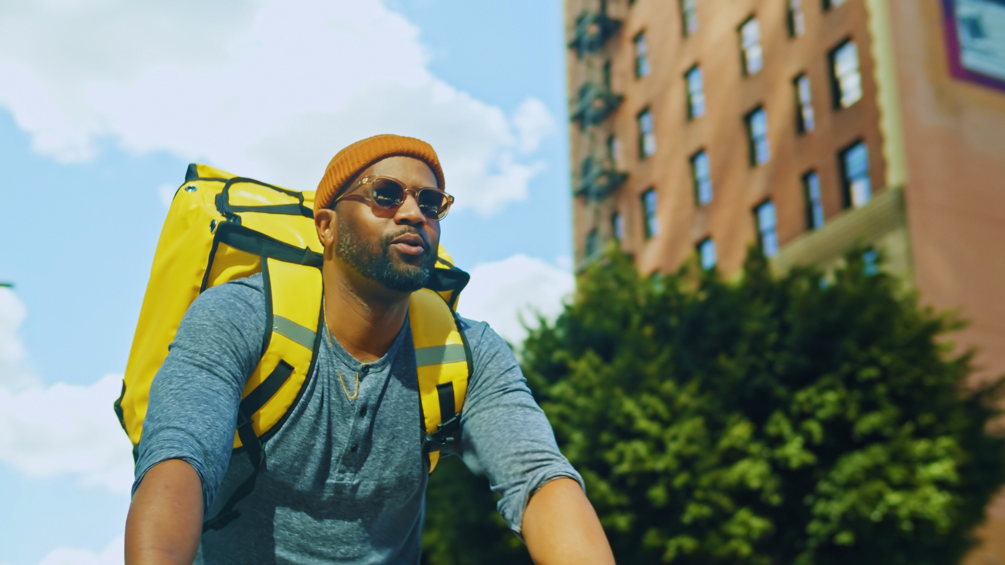 A man riding a bicycle while delivering food, wearing a backpack, representing a gig economy worker such as an Uber Eats or DoorDash driver.