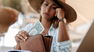 Worried woman looking at a nearly empty wallet with a single dollar bill, symbolizing financial stress and concerns about IRS tax debt and bankruptcy in 2026.